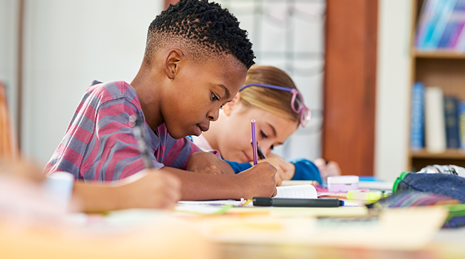 Två skolbarn skriver i ett skrivhäfte.
