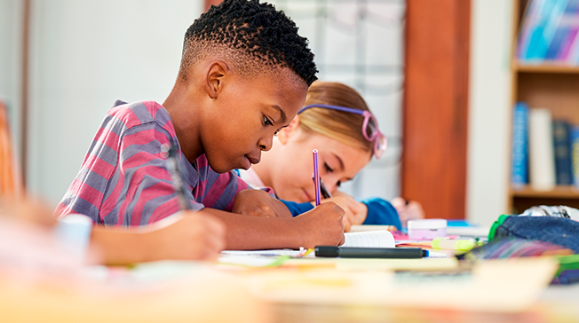 Två skolbarn skriver i ett skrivhäfte.