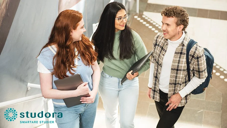 två tjejer med laptops pratar med en kille med ryggsäck i en trappa