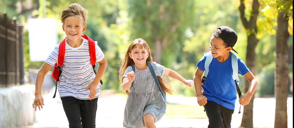 Tre glada skolbarn springer.